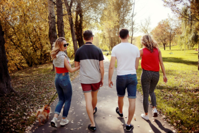 Groepje vrienden werken aan hun mentale gezondheid en gaan zonder jas een wandeling maken in het park terwijl de zon schijnt