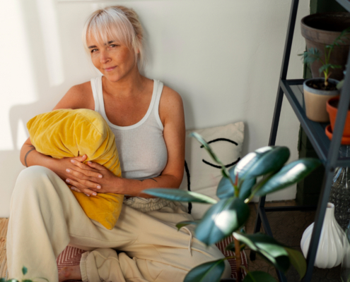Vrouw zit met een geel kussen op de grond terwijl ze laat zien hoe het leven met chronische pijn gaat