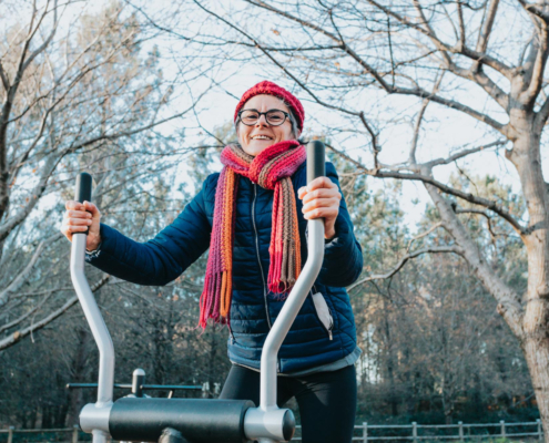 Vrouw met een muts op doet een work out op een crosstrainer in het park en werkt aan haar Goede voornemens.