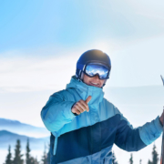 Een man staat in de sneeuw en heeft in zijn ene hand ski's vast en met zijn andere hand steekt hij zijn skiduim op.