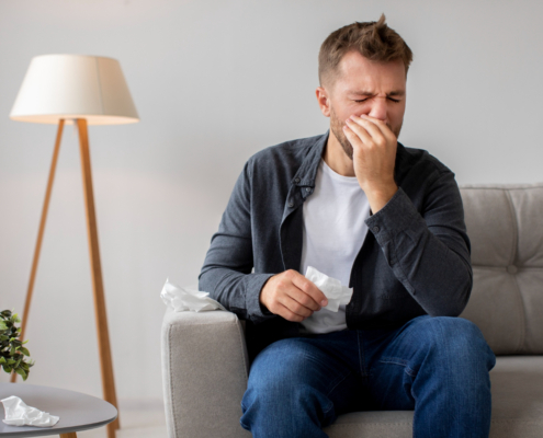 Man met hooikoorts op zit op de bank en veegt zijn neus af aan een zakdoek