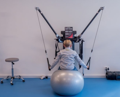 Kind heeft kinderorthopedie, zit op een bal en doet een krachtoefening.