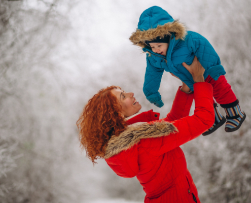 Vrouw in een rode jas heeft geen last van Rugpijn in de winter en tilt haar kind in een blauwe jas op.